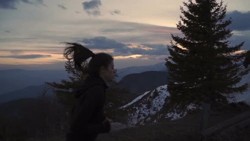 Determined Female Runner Aimed To Reach Mountain Top. Sunset Sky in Bright Colors and Dark Clouds