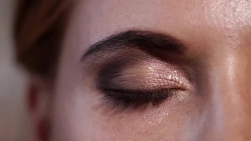 Une jolie femme ouvre ses yeux verts avec du maquillage, en très gros plan