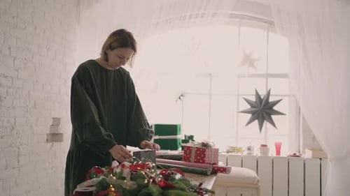 Woman wrapping Christmas presents in a bright room