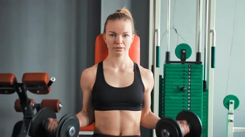 Sporty Young Woman Exercising with Dumbbells in the Gym