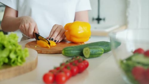 Woman Cuts Yellow Pepper on Wooden Board
