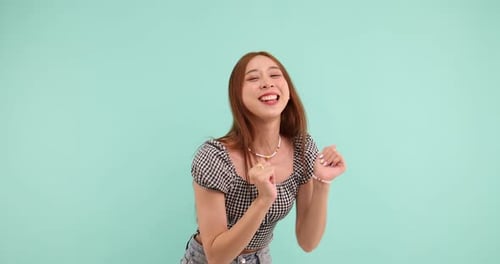 Feliz mujer asiática despreocupada bailando y mirando a la cámara sobre fondo verde