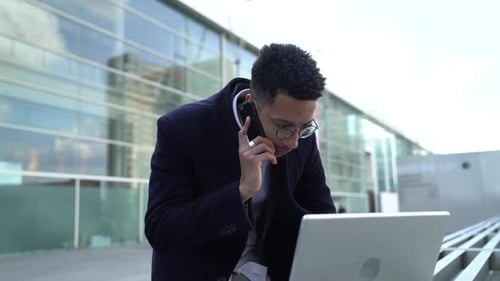 Man Talking on Phone Working on Laptop Outdoors