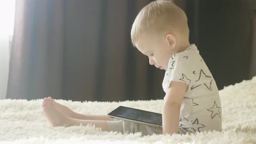Child Sits with Tablet at Home During Daytime