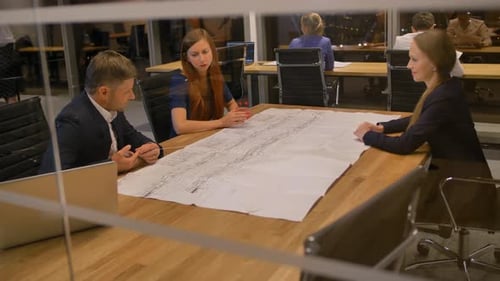Team Reviewing Blueprints in Modern Office at Night