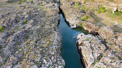 Schmaler Gebirgsfluss, der durch eine felsige Landschaft fließt, tief in Steine gehauenes Bachbett