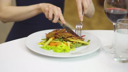 Eine Dame in einem Abendkleid isst Schweinefleisch mit Gemüse mit einer Gabel und einem Messer.
