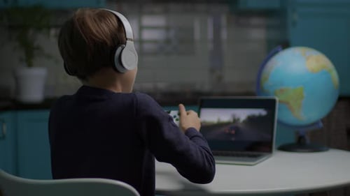 Schuljunge spielt Videospiel auf Laptop mit Joystick und sitzt zu Hause