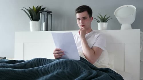 Thoughtful Man Reads Documents in Bed