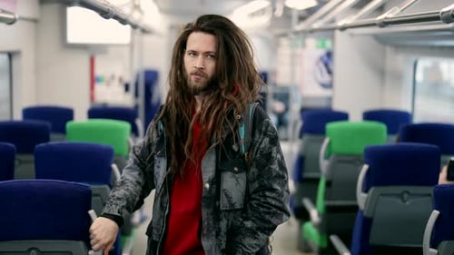 Hombre hipster en tren suburbano de pie y mirando a cámara Retrato medio de pasajero masculino
