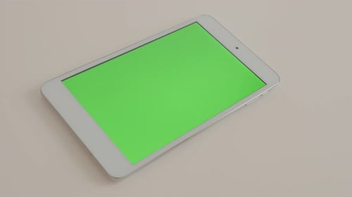 Silver tablet computer on white reflective background displaying chroma green screen 4K 2160p Ultr