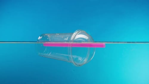 Schwimmendes Plastikglas mit einer Cocktailröhre im Meer, die Müll in den Fluss oder See wirft