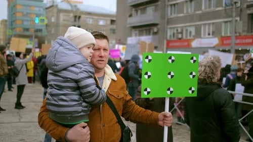 Man Holds Child and Protest Sign in Urban Area