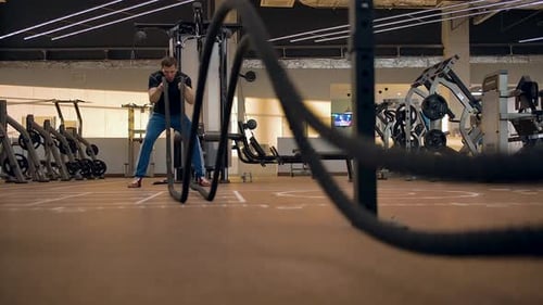Young Caucasian Sportsman Trains with Ropes in the Gym