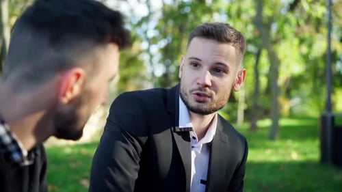 Nahaufnahme Porträt zweier junger Männer, die im sonnigen Sommerpark im Freien sprechen
