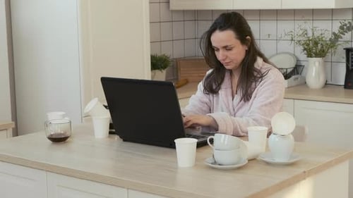 Woman Working at Computer in Kitchen at Home