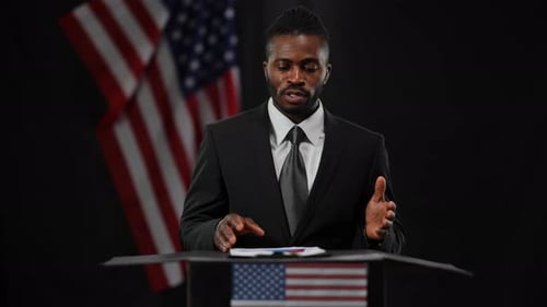 Man Speaks at Podium with American Flags