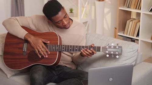 Young Man Plays Guitar on Sofa at Home