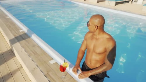 Handsome African Man Enjoying Drinking Cocktail in the Swimming Pool