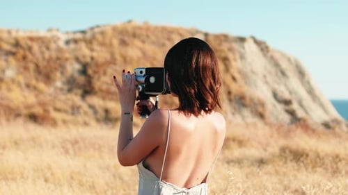 Woman Filming with Vintage Camera on Cliffside