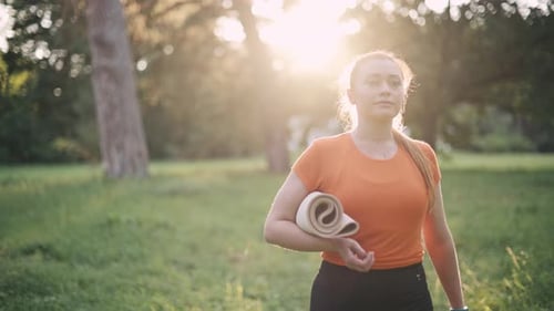 Woman Walking with Yoga Mat in Park at Sunset