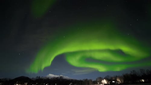 Northern Lights Taking Up Whole Sky with Lit Cabins Down Below and Mountains