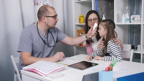Friendly Doctor Talks with Patients Mom and Her Daughter. The Doctor Measures the Temperature of the