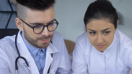 Close-up of Two doctors, a Man and a Woman, Looking at a Tablet screen or Working at a Computer