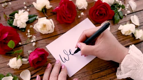 Writing WEDDING on a card near flowers close up