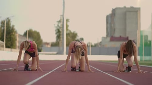 Three Female Track and Water Athletes Start the Race at the Stadium in Running Pads at a Sprint