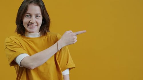 Portrait of Pretty Young Woman Pointing Sidewards and Smiling with Satisfaction