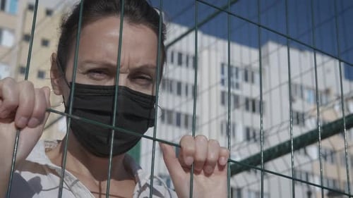 Woman Holding Fence While Wearing a Face Mask