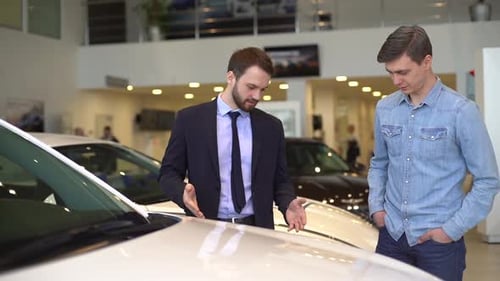Professional Car Salesman Telling Interested Buyer About Car in Auto Dealership.