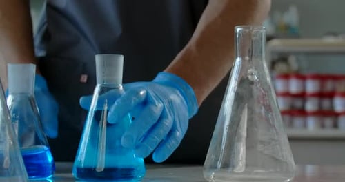 Gloved Hand Swirling Blue Liquid in Lab Beaker