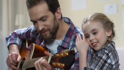 Man Plays Guitar with Child Leaning In Close
