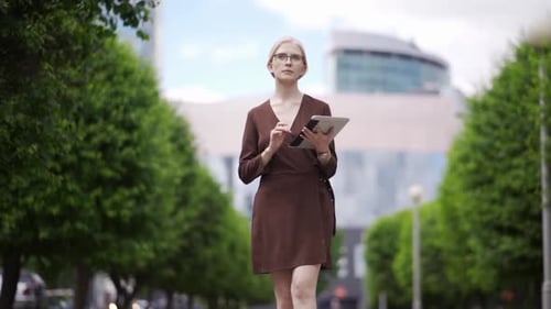 Woman Uses Tablet While Walking in City Park