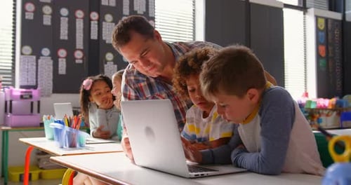 Side view of Caucasian male teacher teaching schoolkids on laptop in the classroom 4k