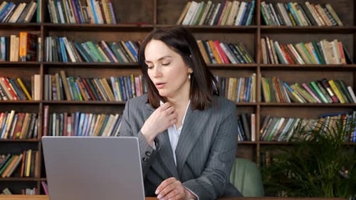 Woman Adjusts Blouse At Desk in Front of Laptop