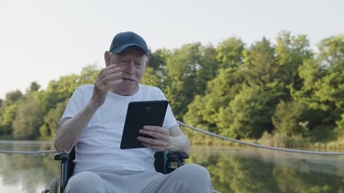 Senior Man Using Tablet in Wheelchair by Lake
