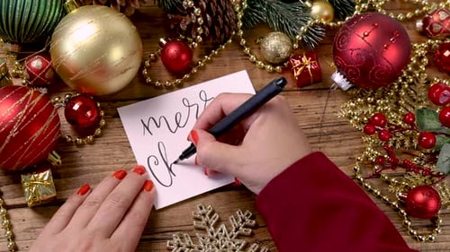 Writing Merry Christmas Card Surrounded by Ornaments