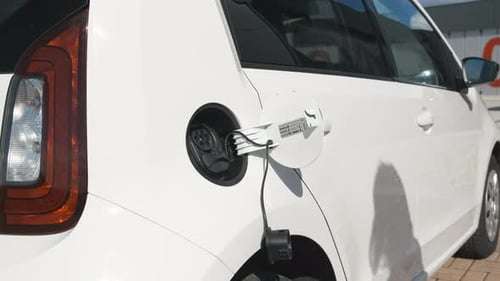 Close Up Womans Hand Inserts an Electric Plug Into the Car to Charge at Sunny Day