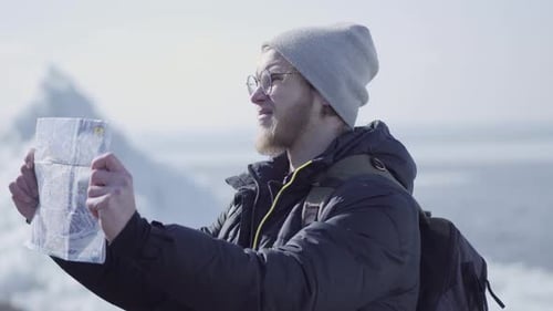 Portrait of Young Blond Bearded Handsome Man Wearing Warm Jacket and Hat Standing on the Glacier