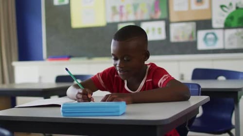 Boy Writing at Desk in Classroom