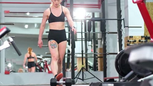 Fitness a Muscular Female Athlete Trains in the Gym with Heavy Dumbbells
