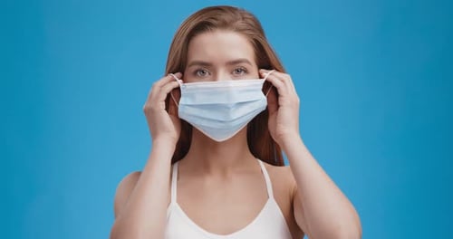 Social Distancing and New Normal. Studio Portrait of Young Woman Putting on Protective Medical Mask