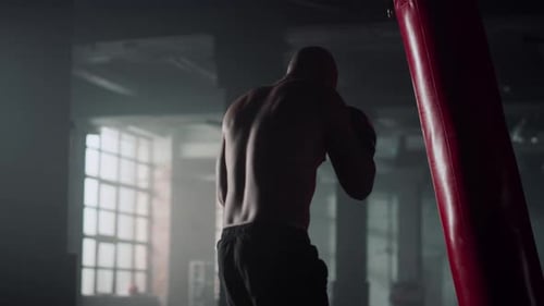 Muscular Man Boxing with Punching Bag in Gym