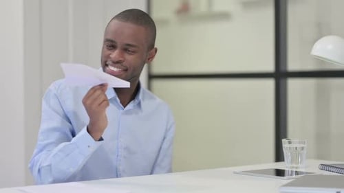 Smiling Young Adult with Paper Airplane at Desk