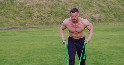 Muscular Man Training with Resistance Bands Outdoors