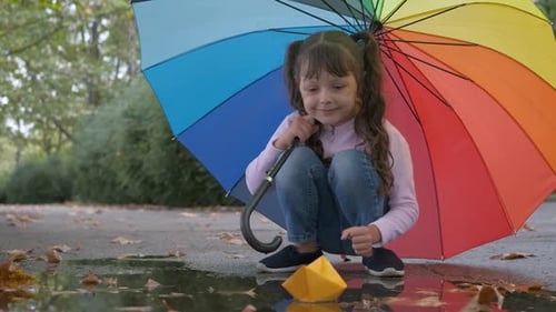 Child Plays with Paper Boat Under Umbrella