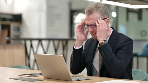 Stressed Young Businessman with Laptop Having Headache in Office